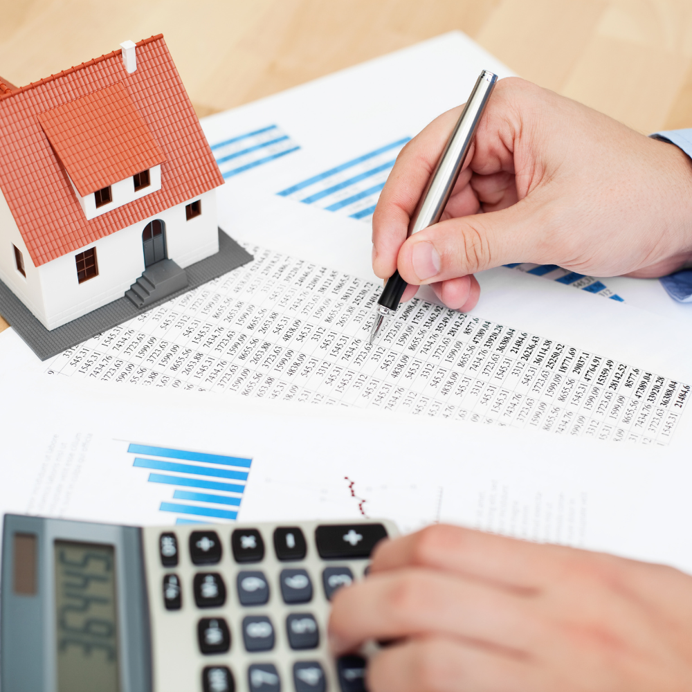 miniature house on a desk with papers and calculator and person looking at numbers